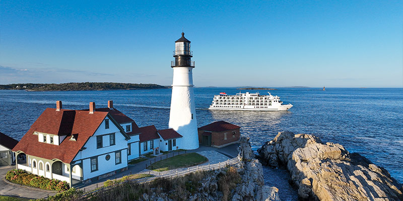 American Cruise Lines ship passing by a lighthouse and home off the coast of Maine