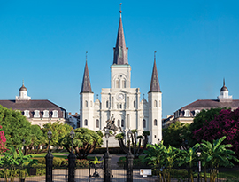 St. Louis Cathedral in New Orleans with lush gardens, a statue, and clear blue sky, highlighting a cruise excursion destination.