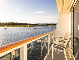 The private balcony of stateroom on American Cruise Lines' American Maverick, featuring outdoor lounge chairs and panoramic views of scenic coastal waterways.