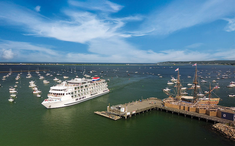 The American Glory cruise ship is docked at a wooden pier on a clear, sunny day, highlighting the vessel's multi-deck, modern white design.