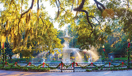 White fountain in a park surrounded by oak trees and holiday decorations in warm afternoon light.