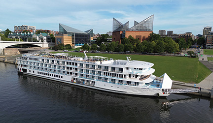 A small American Cruise Lines river ship docked by a park.