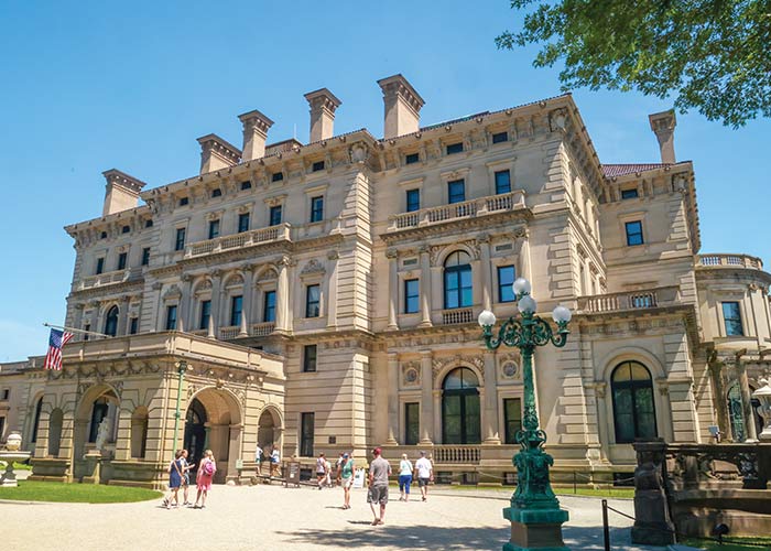 Historic Gilded Age mansion, The Breakers, a large tan building with cruise line guests, under clear blue sky.