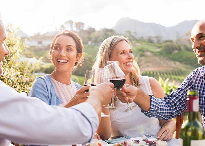People toasting with wine outdoors at the Olympic Cellars Winery in Port Angeles, surrounded by vineyards and mountains.