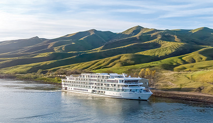 Small American Cruise Lines cruise ship sailing on a river with green hills in the background.