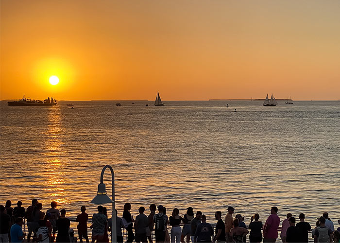 Sunset over Key West, FL with sailboats and a crowd watching from the shore.