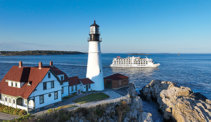 An American Cruise Lines small ship sailing past Portland Headlight, a historic New England lighthouse along a rocky coastline during an all-inclusive coastal cruise.