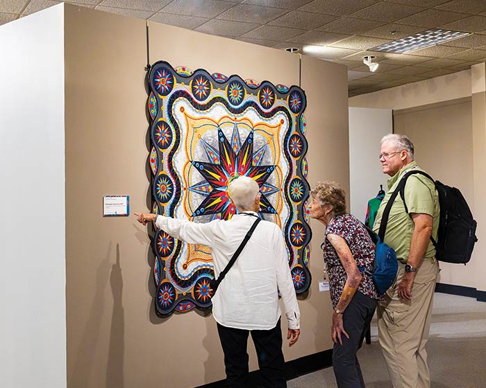Three cruise guests admire a colorful quilt in a museum, part of an American Cruise Lines excursion.