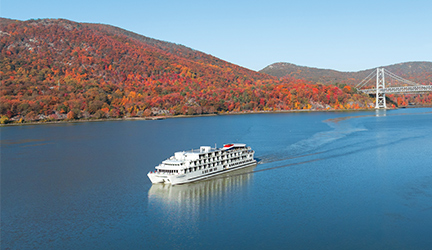 Hudson River fall foliage cruise ship sailing past autumn-colored mountains near a bridge in New York.