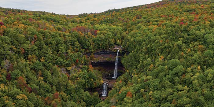 Aerial view of a Hudson Valley waterfall surrounded by dense forest with early fall foliage in the Catskill Mountains.