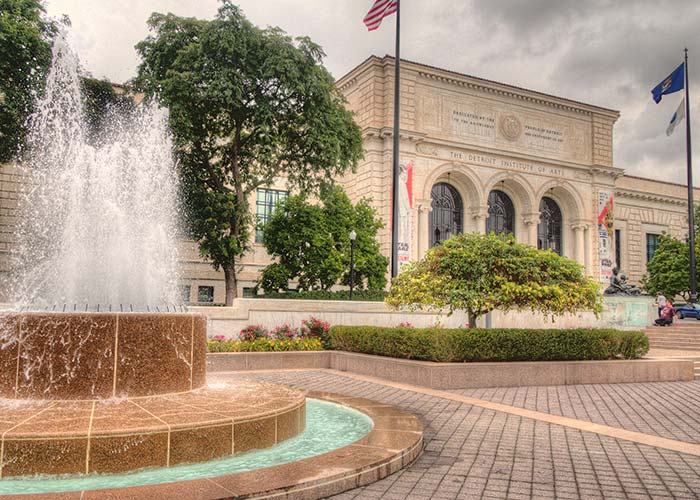 Fountain in front of a historic stone building with arched windows and flags in port city, Detroit.