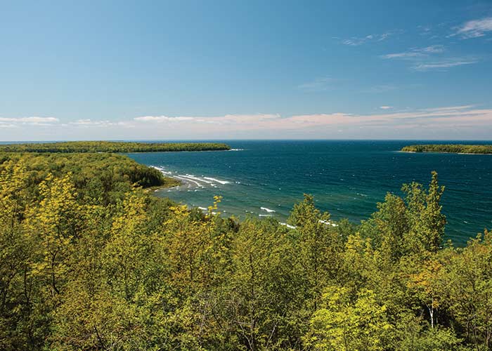 Elevated view of a green shoreline and blue water with trees and a distant horizon in port stop, Green Bay, WI.