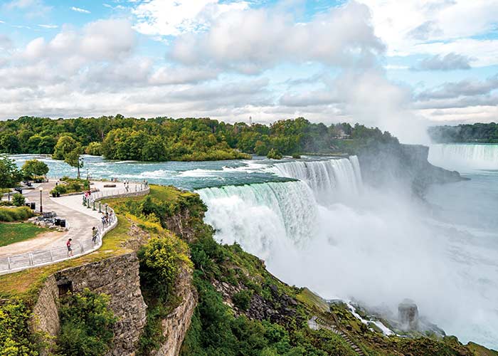 Niagara Falls with cascading water, mist rising, and a viewing area with people along the edge.