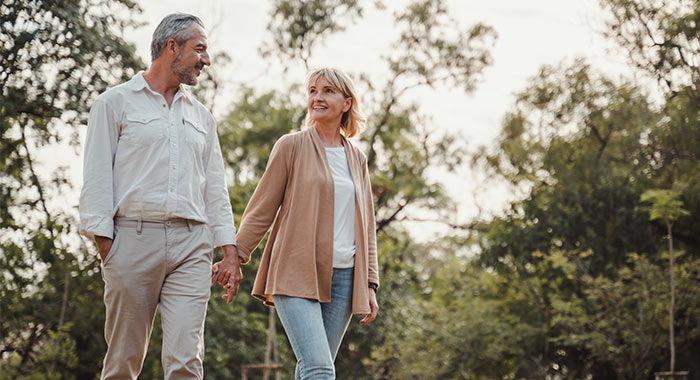 An older man and woman walking hand in hand outdoors in a park, smiling and enjoying a peaceful nature setting in St. Augustine.