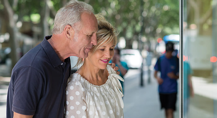 Older couple standing close together and looking into a shop window along a tree-lined street in St. Augustine during a shore excursion