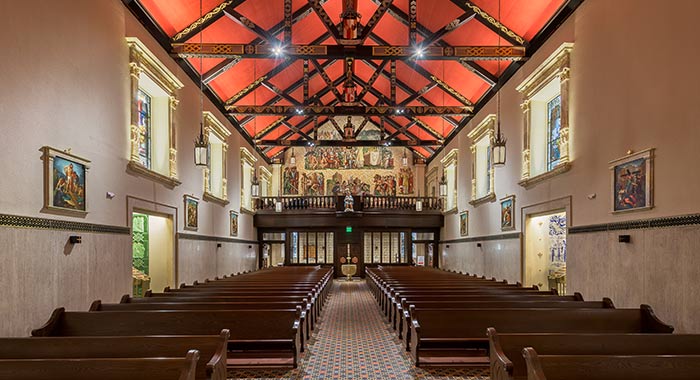 Interior historic Cathedral Basilica of St. Augustine with wooden pews, patterned tile floor, and a painted altar beneath exposed wood beams.