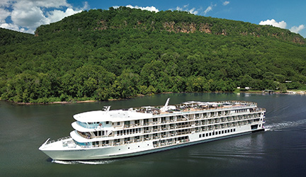 An American Cruise Lines ship sails along the calm Tennessee River with forested hills rising in the background.