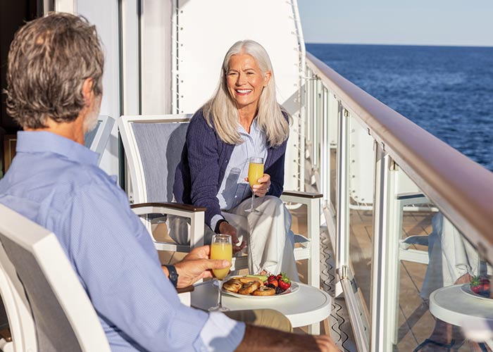 Couple seated at a small outdoor table on a private balcony with drinks, overlooking the water.