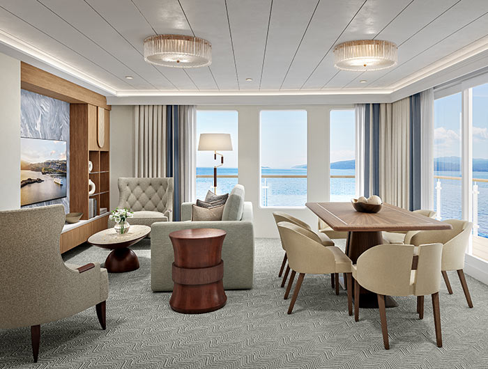 Bright suite interior with large windows, dining table, sitting area, and neutral-toned furnishings overlooking the water.