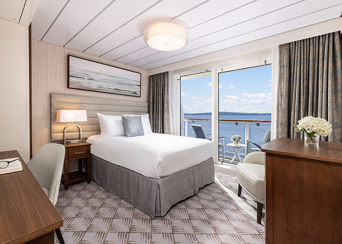 Compact bedroom with bed, nightstand, desk, and large window showing water view outside.