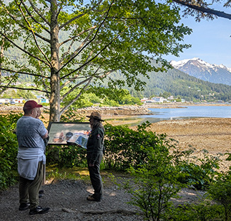 Snow-capped mountains in the distance above a lake with a Guide speaking to guests.