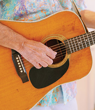 Man playing acoustic guitar, wearing a colorful shirt, part of American Cruise Lines onboard entertainment.