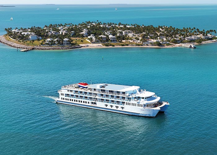 An aerial view of boats docked in a marina in St. Petersburg with the bright blue Gulf Coast waters spanning for miles in the distance. There are several buildings and trees on the shoreline.