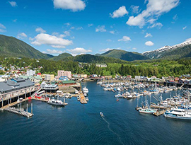 Scenic harbor with small cruise ships, surrounded by mountains and lush greenery, under a blue sky.