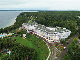 Aerial view of the Grand Hotel on Mackinac Island near a lush, green coastline and Lake Huron cruise port.