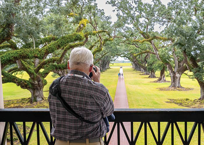 The historic St. Francisville landmark the Rosedown, a yellow house with bright green shutters and two-story white pillars with a brick pathway surrounded by perfectly trimmed bushes and large trees leading to the red door. 
