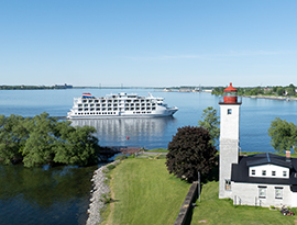 American Patriot cruise ship on one of the Great Lakes, surrounded by scenic shoreline with trees and houses, under a clear blue sky.