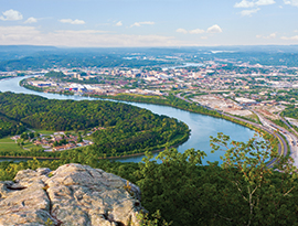 Aerial view of a river winding through a lush landscape with a city in the background, along American Cruise Lines' Great Smoky Mountains Cruise route.
