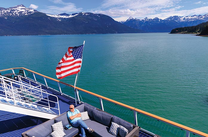 Man relaxing on a cruise ship deck in Alaska, surrounded by scenic mountains and calm waters.