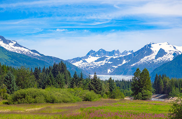 Buildings stand upon a foundation on tall stilts above the Gastineau Channel in Juneau, where a large mountain covered in thick forest is in the near distance.