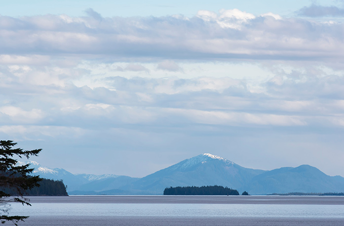 Scenic view of calm waters and distant snow-capped mountains in Metlakatla, AK.