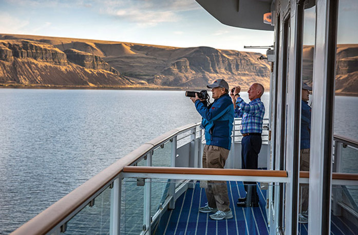 Guests photographing canyon scenery from a balcony during a Snake River cruise.