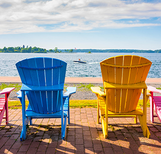 Colorful Adirondack chairs facing the St. Lawrence River in Clayton, NY with a small boat in the distance.