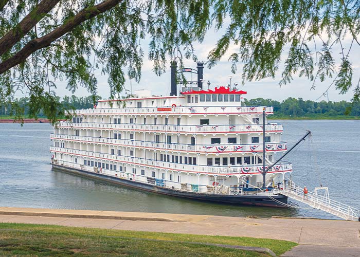 American Heritage, an American Cruise Lines Paddlewheeler decorated with patriotic red white and blue bunting flags on the front railings, docked along the Mississippi River in Paducah, KY letting passengers off from the front of the ship.