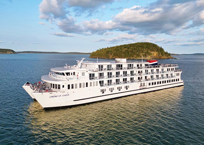 American Eagle, an American Cruise Lines Coastal Cat small cruise ship sailing along an intimate waterway, with green nature landscapes on the shore in the background.