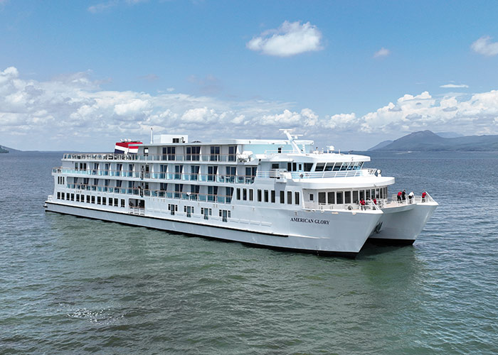 American Glory, an American Cruise Lines Coastal Cat small cruise ship sailing along the Maine coast, with views of small mountains in the distance.
