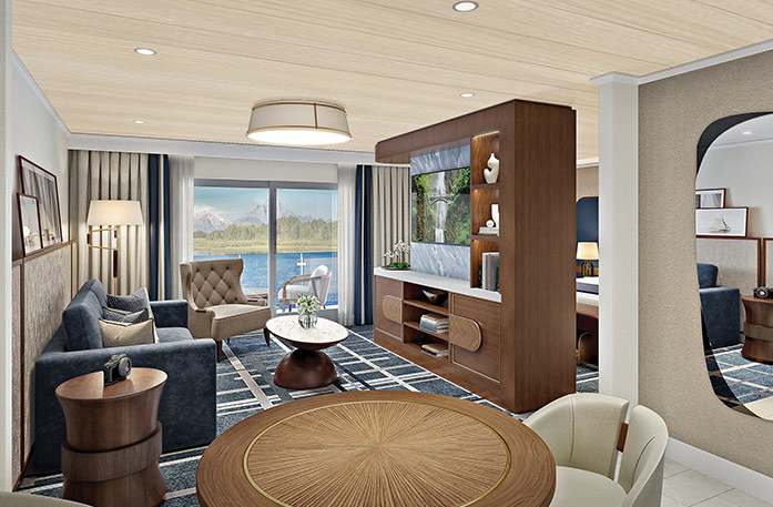 The Grand Suite on American Anthem, with large floor-to-ceiling sliding glass doors leading to a private balcony overlooking the Columbia River. There is a navy blue sofa and a tan armchair facing a large wooden TV stand in the center of the room, with a TV and shelves with decor. 