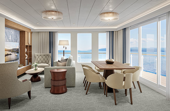 The spacious Signature Suite on American Encore, with floor-to-ceiling glass windows along the back wall overlooking the private balcony and the Columbia River. There is a wooden dining table with six tan chairs around it, a tan sofa and armchair, and a coffee table.