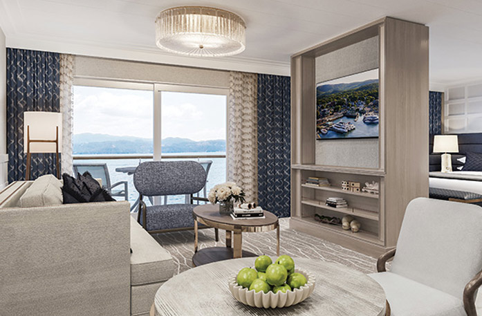 The Grand Suite on American Mariner, with large floor-to-ceiling sliding glass doors leading to a private balcony overlooking the New England coast. There is a tan sofa facing a large wooden TV stand in the center of the room, with a TV and shelves with decor. 