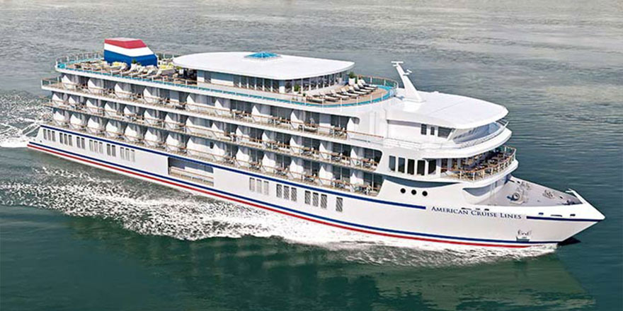 An aerial view of American Patriot, an American Cruise Lines Patriot Class small cruise ship sailing along the New England coast, with views of the shore in the distance.