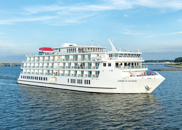 An aerial view of American Ranger, an American Cruise Lines Patriot Class small cruise ship sailing along the Hudson River, with views of the shore in the distance.
