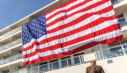 A large, vibrant American Flag hanging on the side of one of American Cruise Lines' cruise ships. 