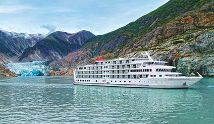The American Constellation cruise ship sailing through the bright blue Alaskan waters alongside mountains and glaciers.