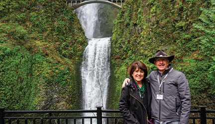 Two older adults posing in front of a waterfall during an American Cruise Lines excursion.