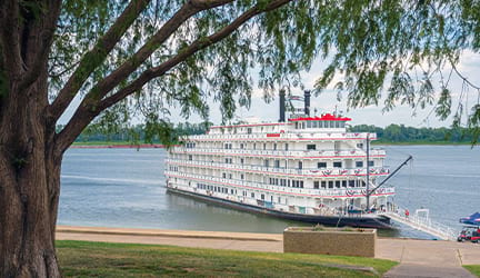 American Heritage, an American Cruise Lines Paddlewheeler decorated with patriotic red white and blue bunting flags on the front railings, docked along the Mississippi River in Paducah, KY letting passengers off from the front of the ship.