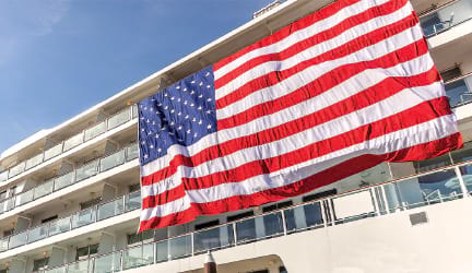 A large, vibrant American Flag hanging on the side of one of American Cruise Lines' cruise ships. 